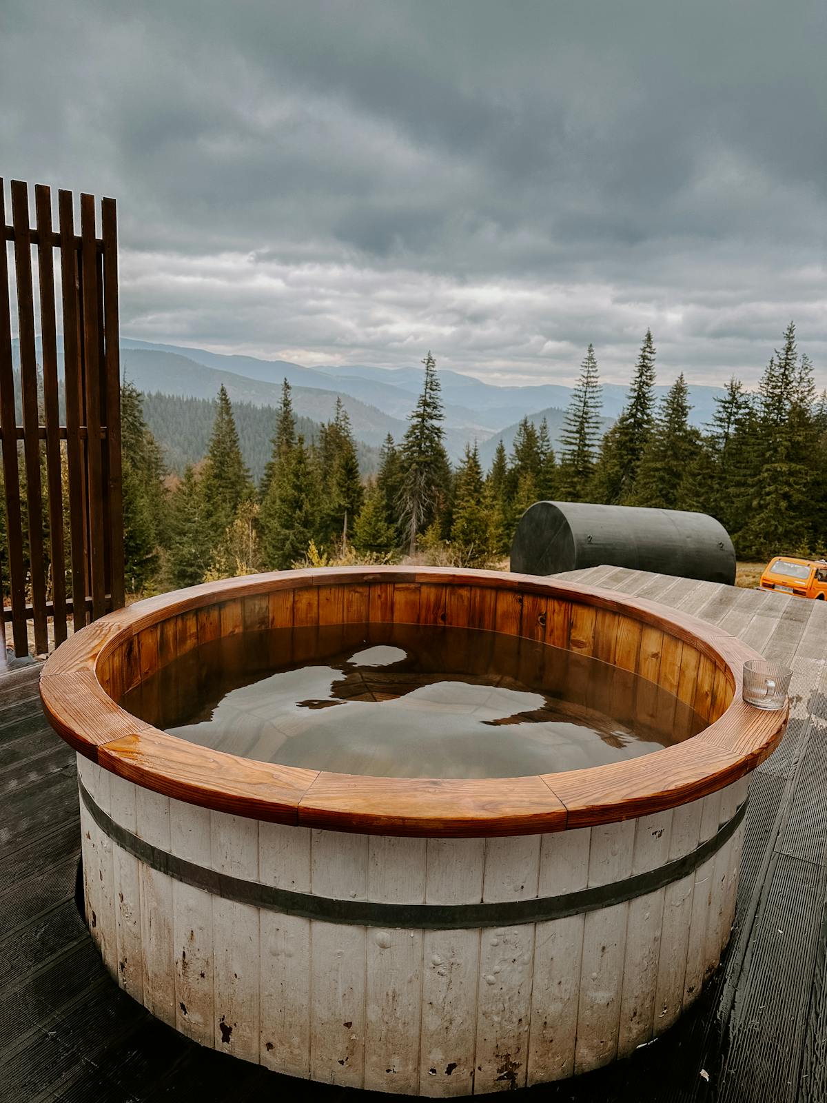 Rustic wooden hot tub on an outdoor deck overlooking a mountain forest view